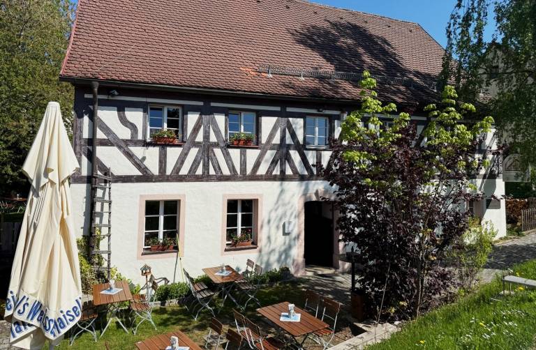 Fachwerkhaus der Zaussenmühle mit Biergarten, Sonnenschirmen und blühendem Baum