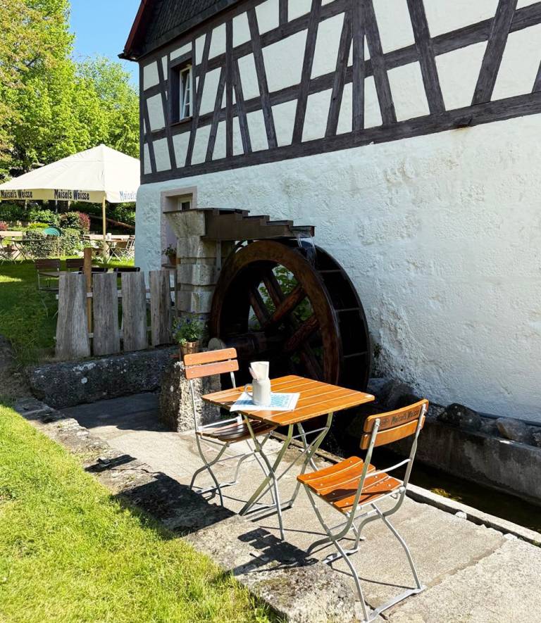 Tisch mit zwei Klappstühlen neben dem hölzernen Wasserrad der Zaussenmühle