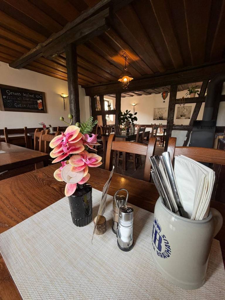 Gedeckter Tisch mit Blumen, Besteckkrug und Menage im Gastraum der Zaussenmühle unter einer Holzbalkendecke