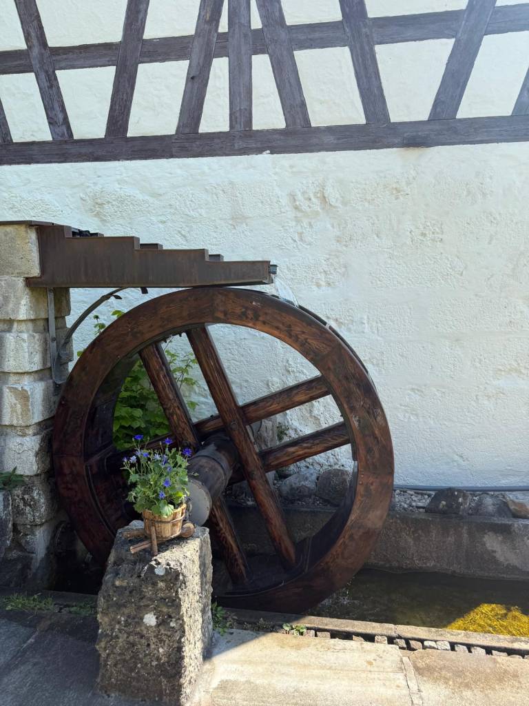 Hölzernes Wasserrad an der weiß verputzten Fachwerkwand der Zaussenmühle in Pegnitz